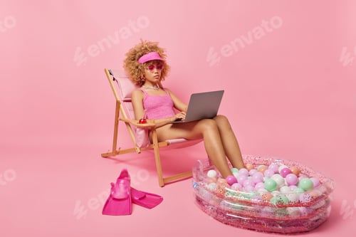 Preview: Serious woman works on laptop computer during summer vacation dressed in swimsuit keeps legs in smal