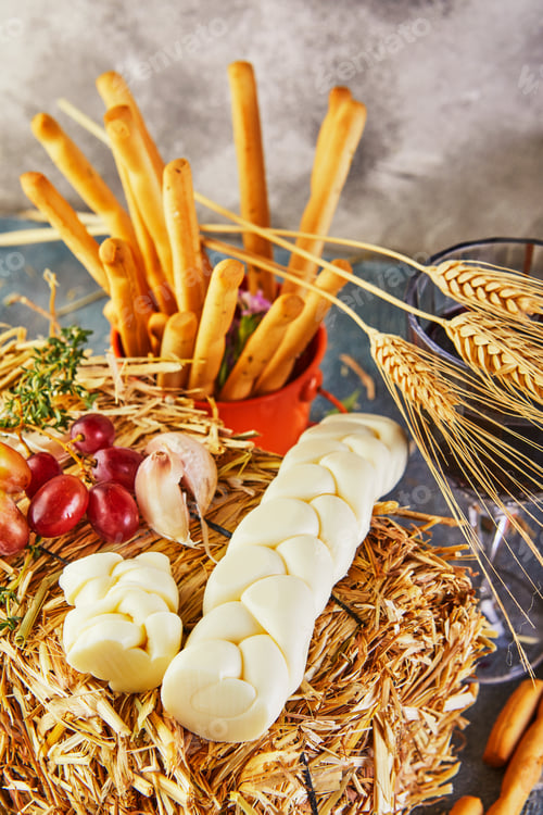 Preview: Pigtail-shaped mozzarella with grapes in the hay with bread ears on a blue background.