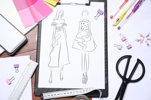 Preview: Sketch of stylish clothes and other fashion designer`s supplies on wooden table, flat lay