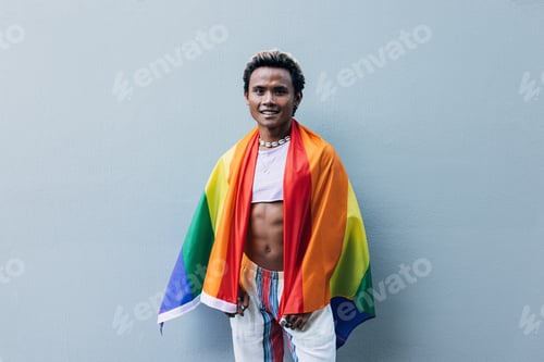 Preview: Young smiling male with LGBT flag at grey wall