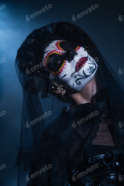 Preview: woman in spooky halloween makeup and black veil posing on dark background with blue light