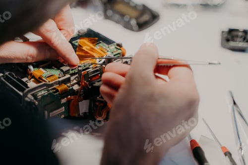 Preview: Professional technician repairs disassembled parts of camera, holds tweezers, works in service