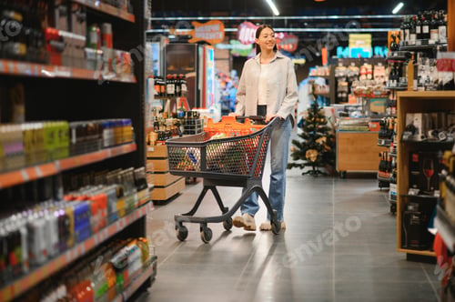 Preview: Young smiling happy woman 20s in casual clothes shopping at supermaket store with grocery cart