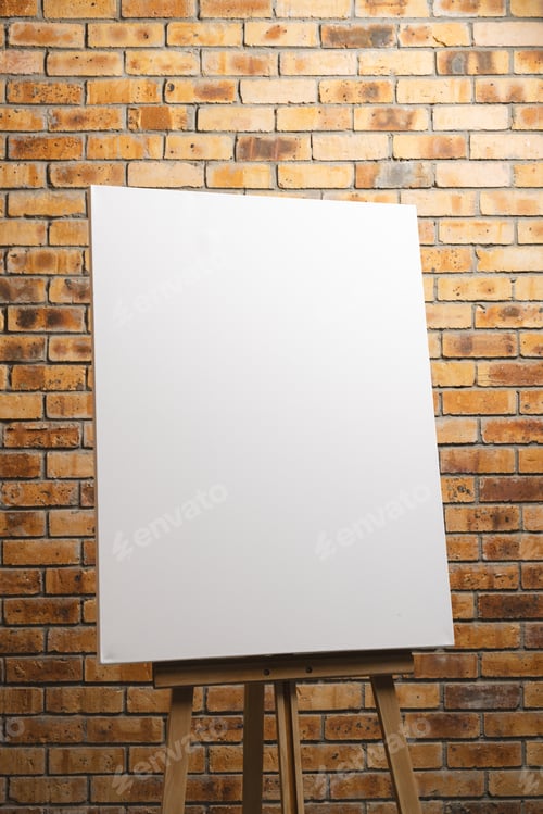 Preview: White canvas on wooden easel and copy space on brick wall background