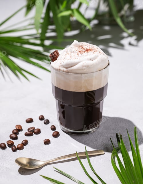 Preview: Iced coffee in a glass with foam on a light background with palm leaves, coffee beans