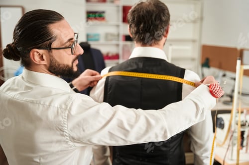 Preview: Focused couturier taking customer body measurements using tape measure
