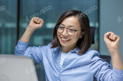 Preview: Asian businesswoman celebrating success while working on a project in office