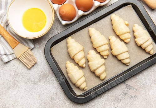 Preview: Baker preparing raw croissants on baking tray for baking