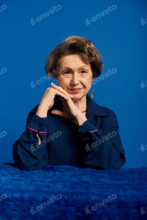 Preview: Exuding grace, a woman in her 60s poses in chic attire with a radiant smile.