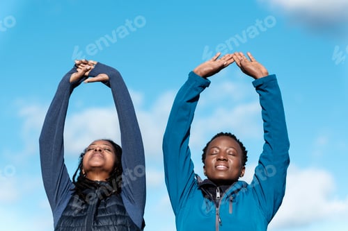 Preview: Two mature black women stretching arms outdoors.