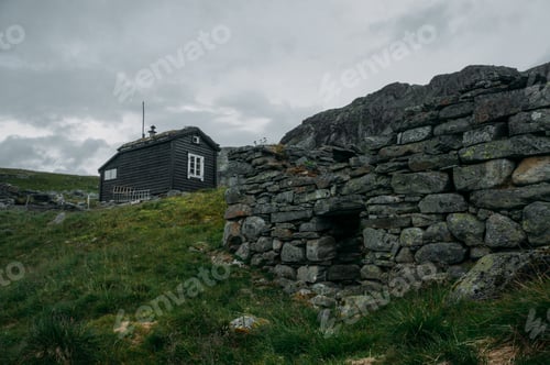 Preview: ruined old stone wall and rural house on background over field with green grass, Norway,