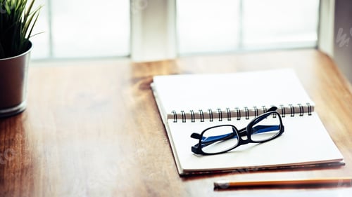 Preview: Open notebook paper and glasses on wood table.