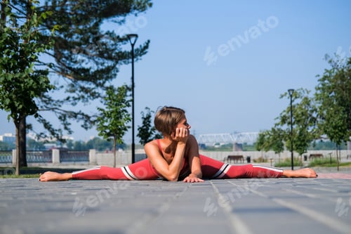 Preview: Young Attractive Woman In Red Sportswear Practices Yoga Exercises Outdoors.
