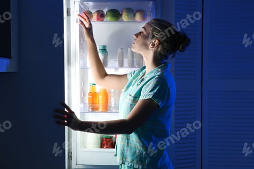 Preview: Woman choosing food from refrigerator in kitchen at night