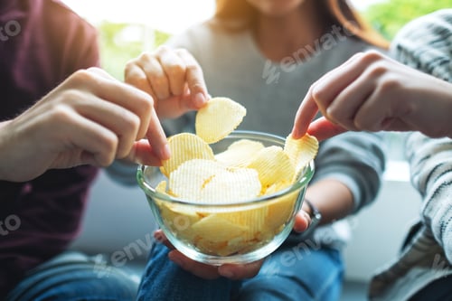 Preview: Closeup image of friends sharing and eating potato chips at home party together