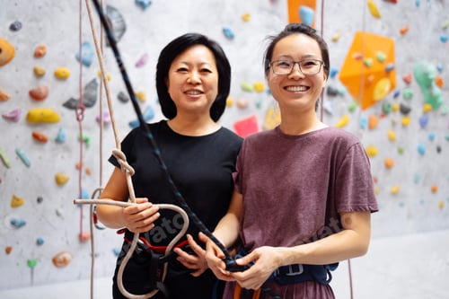 Preview: Smiling Asian women in sportswear posing near the bouldering training wall.
