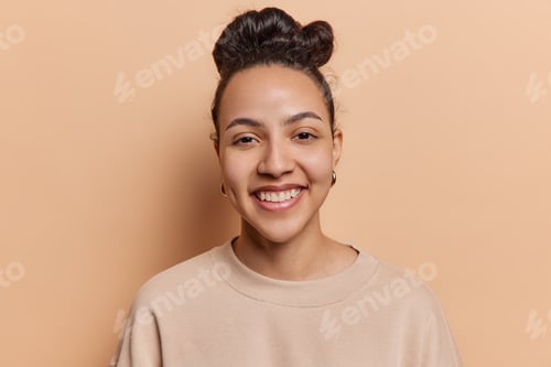 Preview: Portrait of lovely Latin woman with dark hair gathered in bun smiles toothily looks at camera with