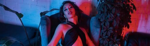 Preview: High angle view of stylish asian woman sitting on armchair in night club with neon light, banner
