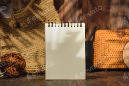 Preview: blank sprial notebook with wicker bag and travel stuff on table with sunlight