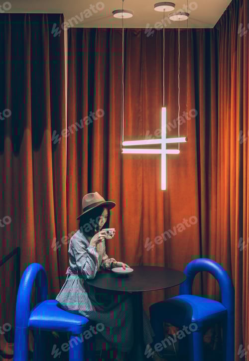 Preview: Woman sitting on blue chair drinking coffee at table