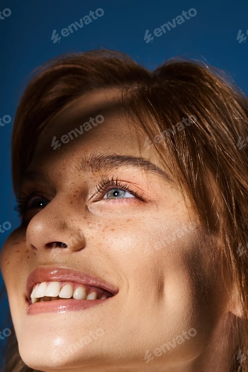 Preview: Closeup beauty portrait of smiling blue eyed woman with freckles on dark blue background