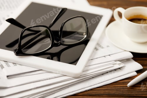 Preview: eyeglasses, coffee cup, digital tablet and newspapers on wooden table