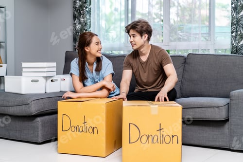 Preview: happy young couple packing stuff clothes, object charity in cardboard box, reused for donate