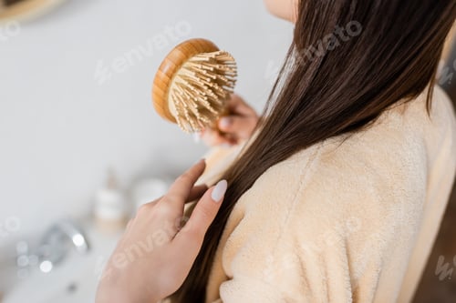 Preview: cropped view of young woman brushing shiny hair in bathroom