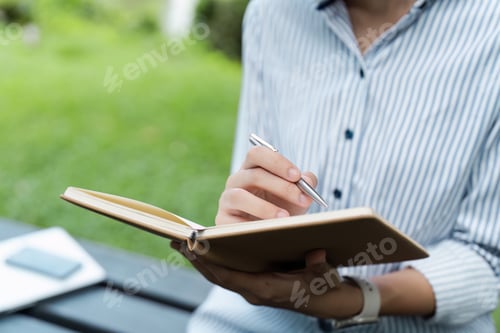 Preview: Close-Up of Person Writing in Notebook Outdoors on a Bench in a Park