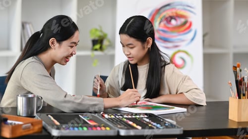 Preview: Asian girl having fun painting with teacher in art class.