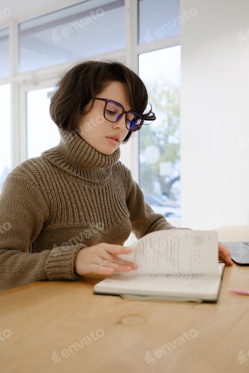 Preview: Woman in glasses focusing on reading at a desk in a bright space