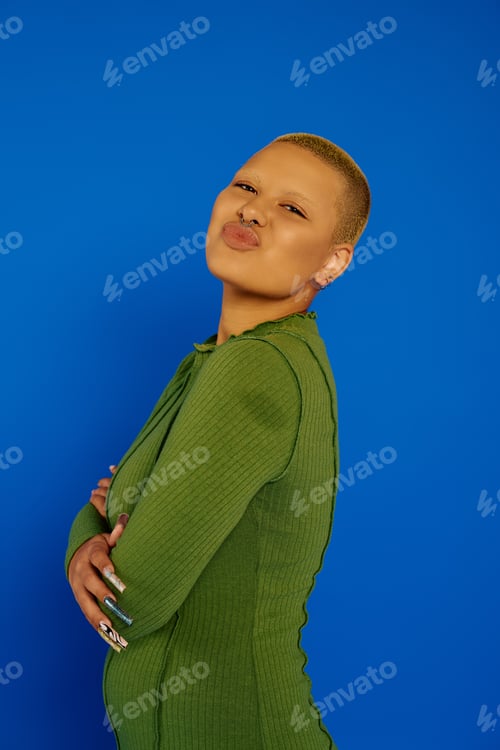 Preview: A young stylish woman poses confidently against a vibrant blue background at a fashion event