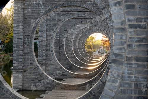 Preview: The architectural detail of a circular brick bridge with sunlight filtering through.