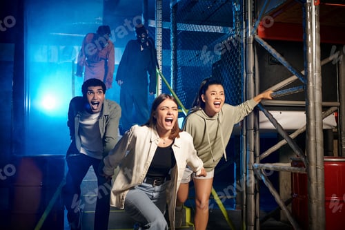 Preview: scared multicultural friends running from freaky people in gas masks and ppe suits in escape room