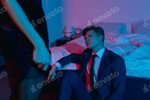 Preview: handsome young man looking at woman in black dress in bedroom while sitting on floor