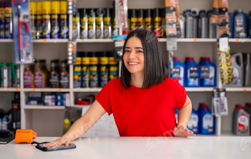 Preview: Young woman smiling while cleaning the counter at an auto parts store