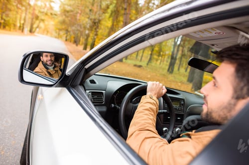 Preview: Smiling bearded male driver reflected in a car mirror in autumn forest