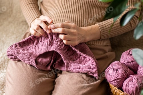 Preview: Close-up of the hands of a young woman knitting needles in a cozy home