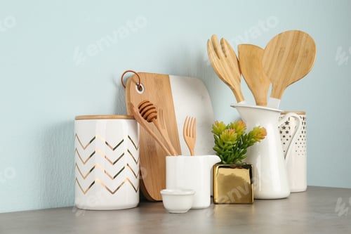 Preview: Potted plant and set of kitchenware on grey table near light wall. Modern interior design