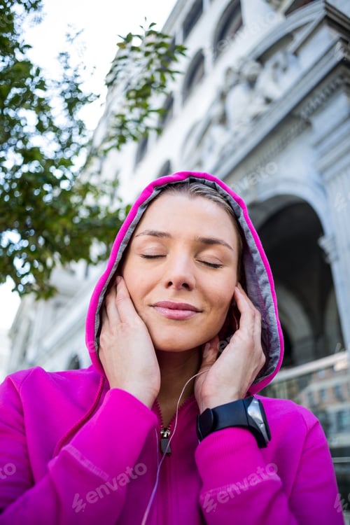 Preview: A woman wearing a pink jacket putting her headphones on a sunny day