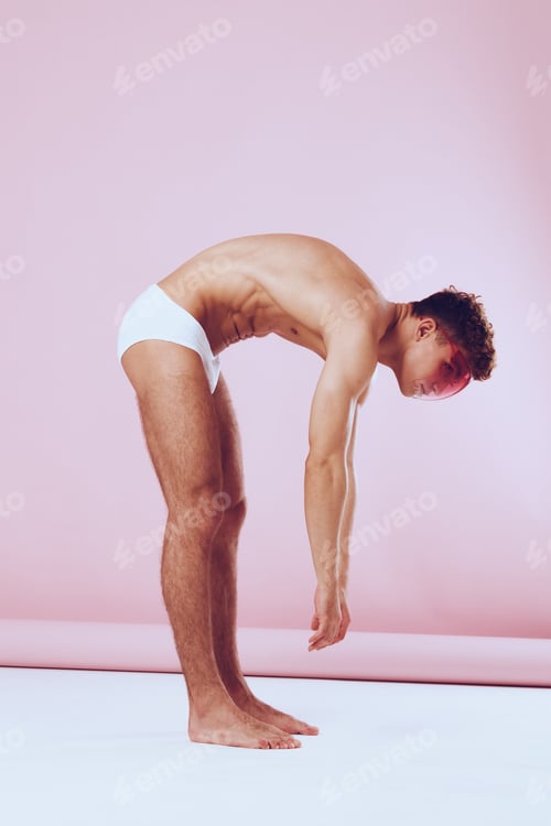 Preview: Athletic young man bending forward, showcasing flexibility and strength against a soft pink