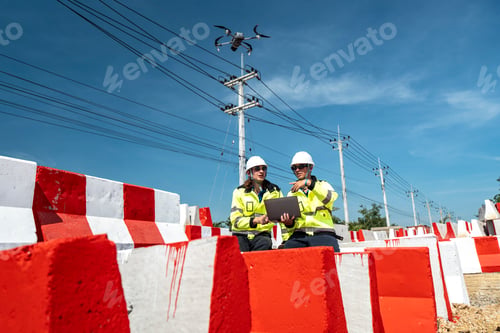 Preview: Two engineers sit amidst red-and white barricades at a construction site.