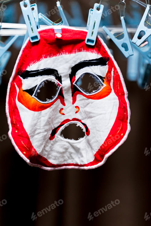 Preview: Vertical closeup shot of a washed theatrical mask hanging from a cable