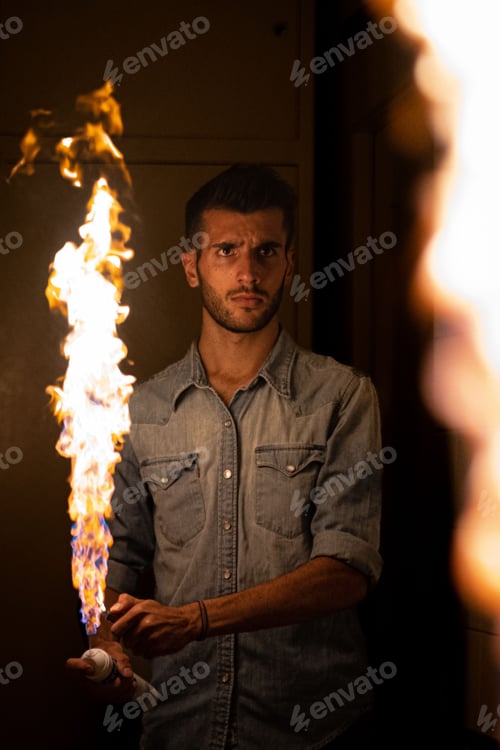 Preview: Adult male standing in a dimly lit room, holding a burning flame in his hand