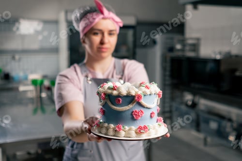 Preview: in a professional kitchen a female baker stands with a finished cake in her hands
