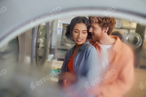 Preview: romantic redhead man hugging and flirting with asian girlfriend in public laundry