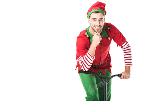 Preview: smiling man in christmas elf costume looking at camera, touching chin and riding push-cycle isolated