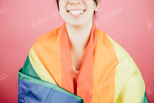 Preview: Woman smiling happily to camera while holding a LGBTIQ flag around her showing pride