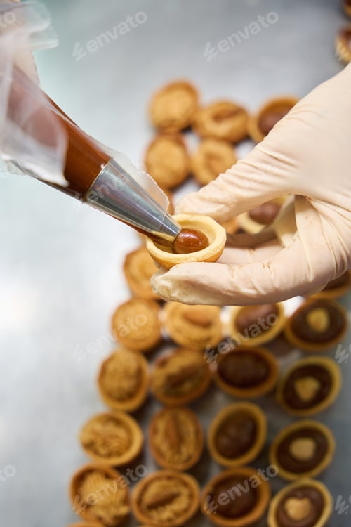 Preview: Confectioner using pastry bag to fill halves of cookies nuts with fudge
