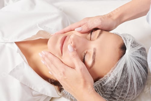 Preview: Beautician massages woman face skin after rubbing moisturizing cream for rejuvenation in clinic
